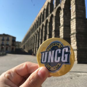 hand holding a UNCG sticker in front of ruins