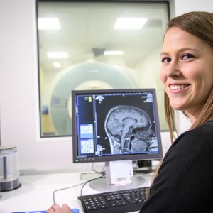 student sits at desk in front of computer displaying brain scan
