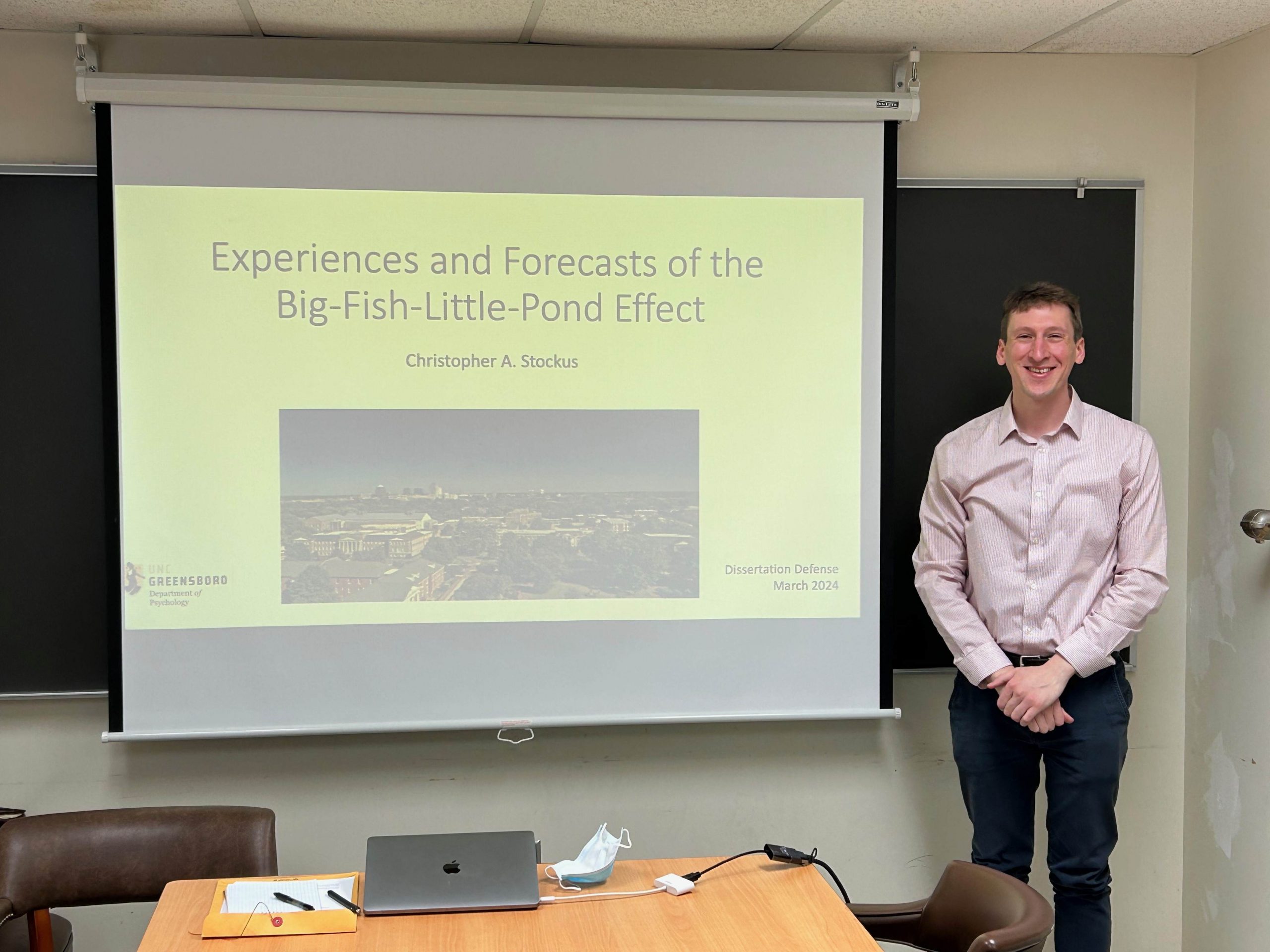 Photo of Chris Stockus in front of the title slide from his dissertation presentation