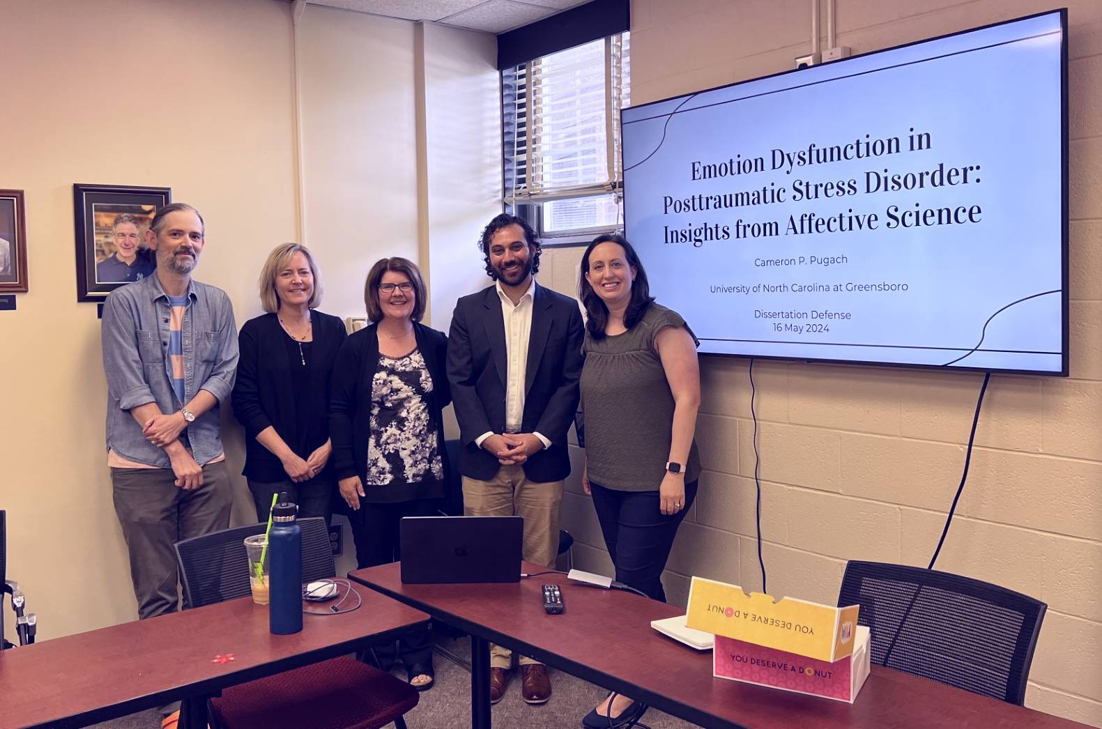 Photo of Cameron Pugach & his committee next to his dissertation title slide