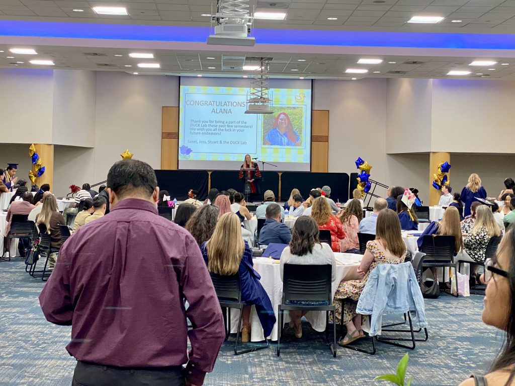 People sitting and standing at the 2025 UNC Greensboro Psychology Department Graduate Recognition Ceremony