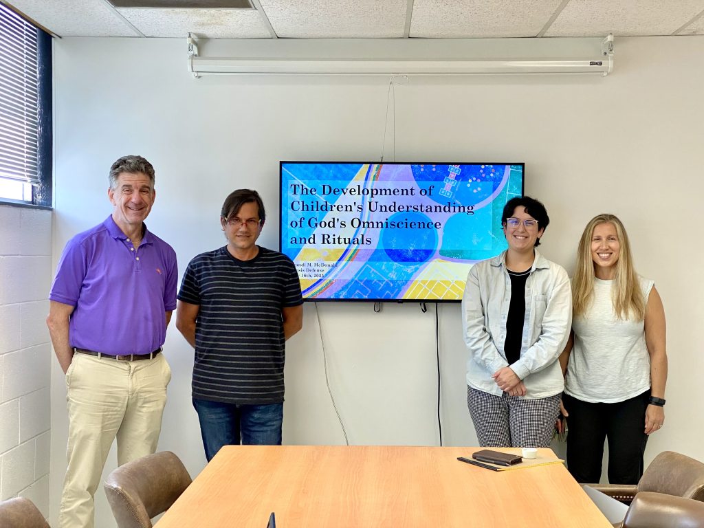 Brandi McDonald with her thesis committee stand in front of her title slide